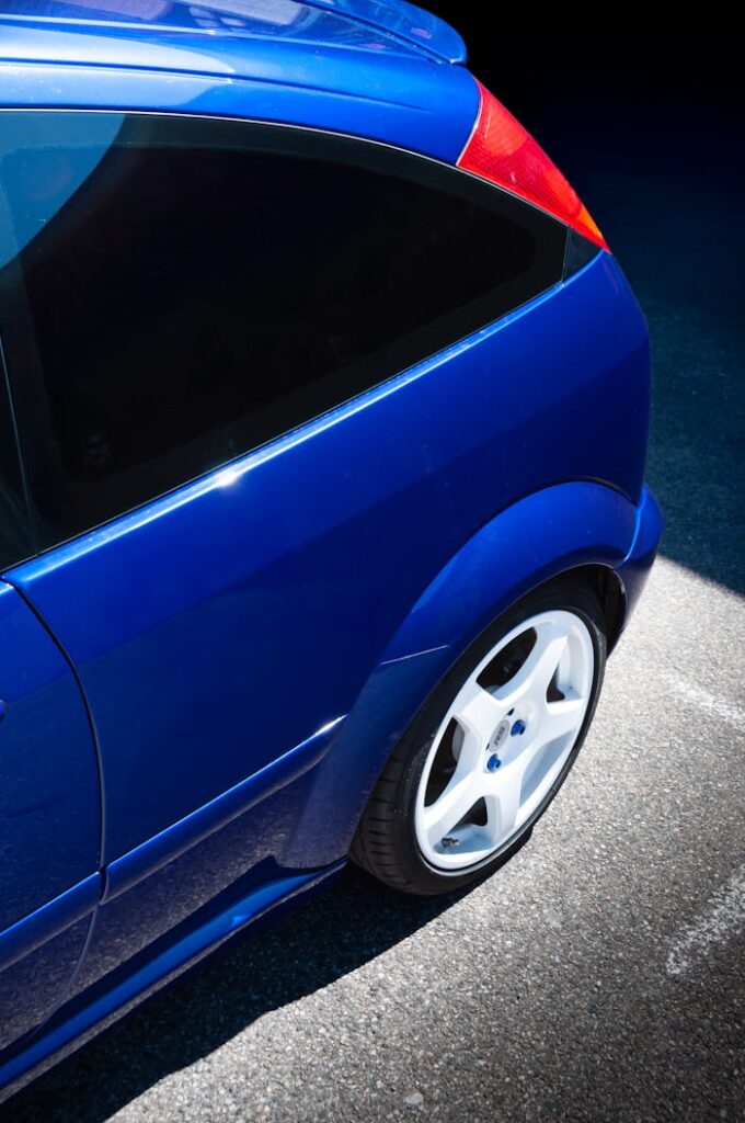 Close-up of a blue sports car with white rims shining in sunlight, outdoors.